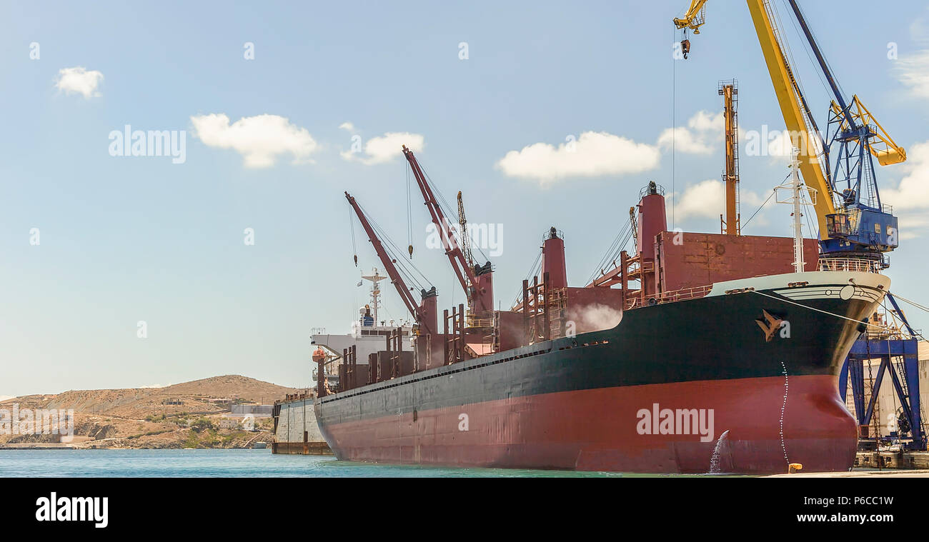 Big bulk carrier with heavy lifts moored in harbour. Stock Image. Stock Photo