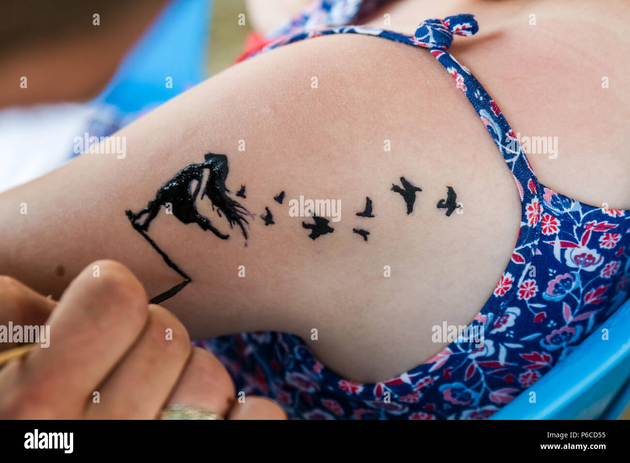 Tattooist making a temporary tattoo on the shoulder of a young girl