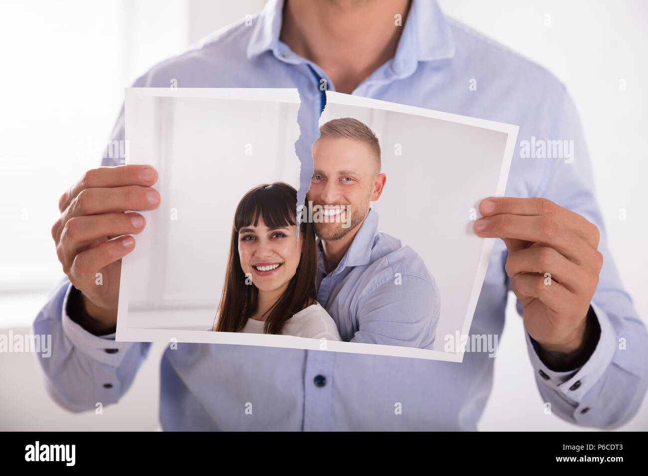 Close-up Of A Man's Hand Tearing Photo Of Smiling Couple In Two Pieces Stock Photo