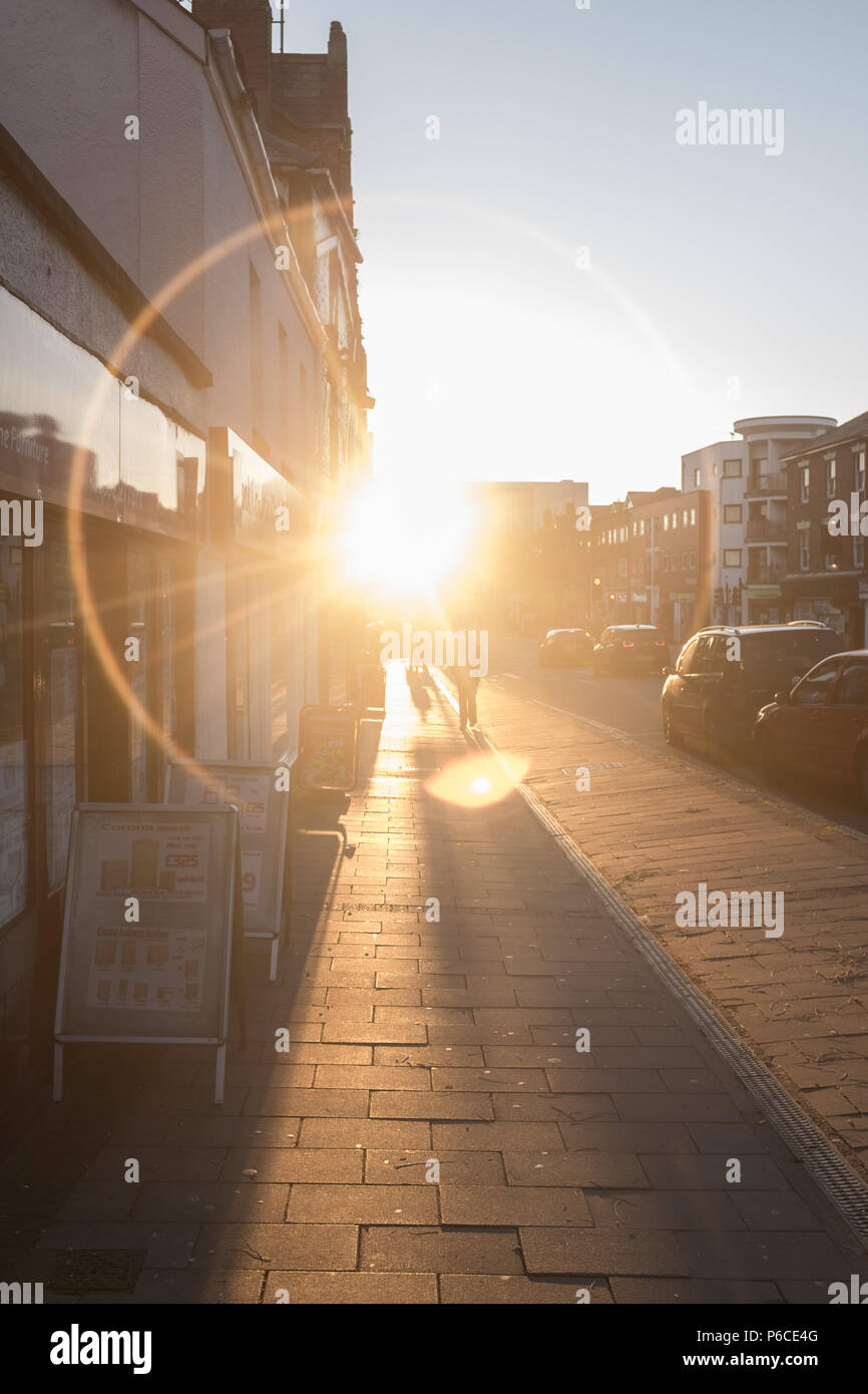 Ring of light shining on pavement through a road down a London street at Sunset as people go about their daily life, Hackney, England, Great Britain. Stock Photo