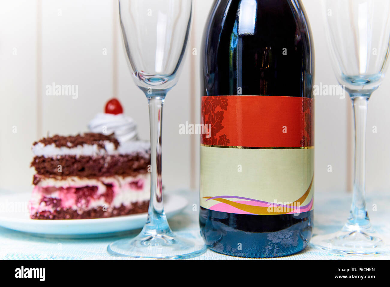 A bottle of red wine on a blurred background of a cake with cherries and wineglass. Stock Photo