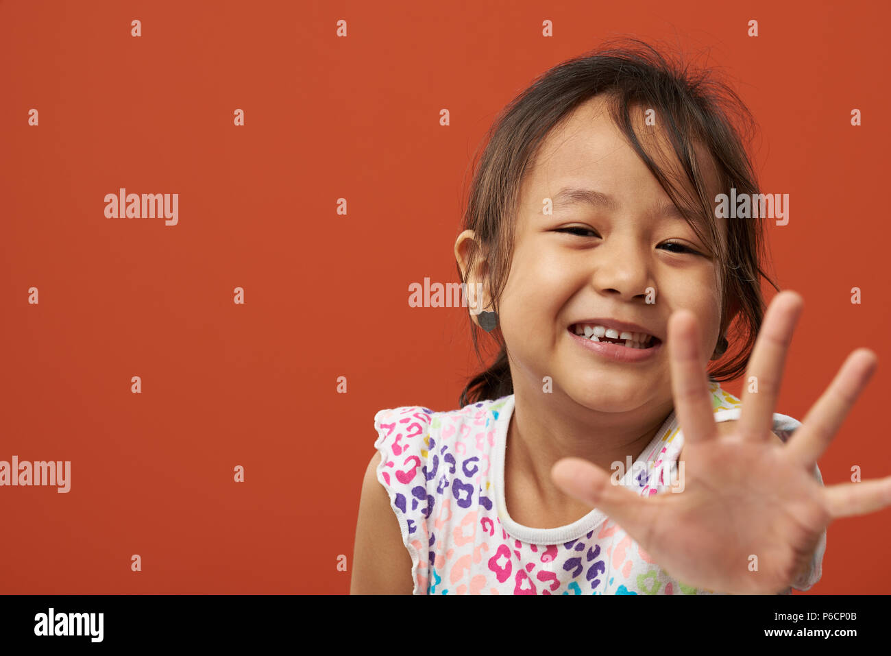 Portrait of smiling girl showing palm hand isolated on orange color