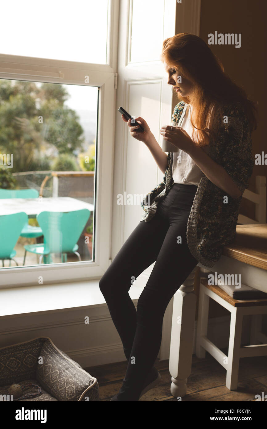 Woman having coffee while using mobile phone Stock Photo