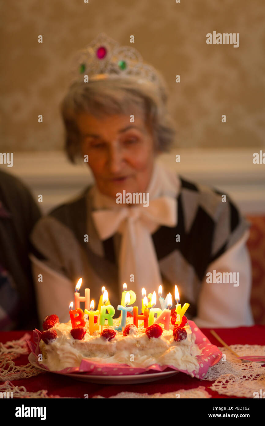 Senior woman blowing out candles on birthday cake Stock Photo
