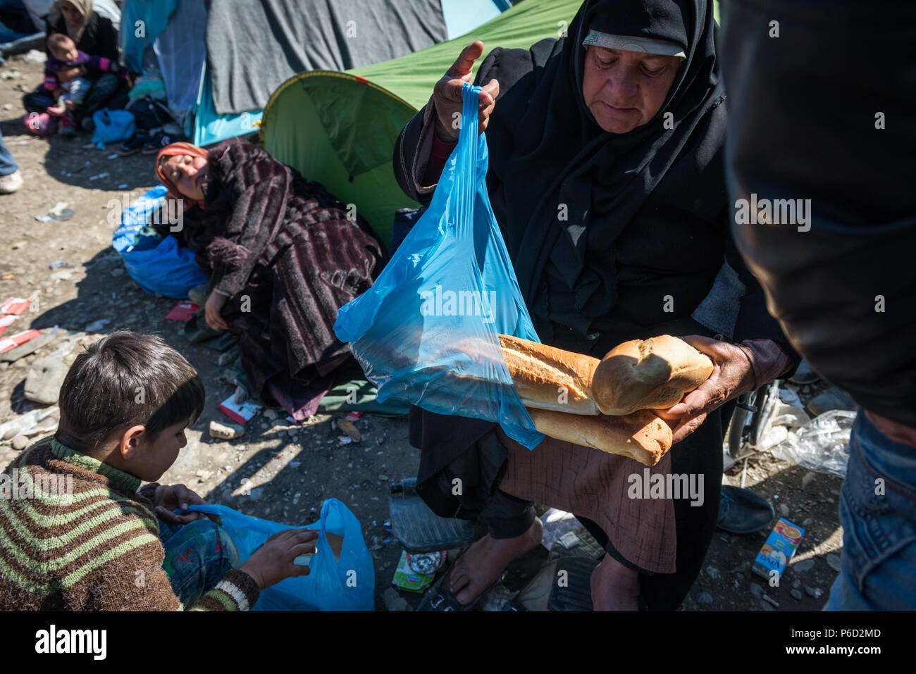 A refugee holds bread provided by humanitarian agencies  as they waits to cross the border at the makeshift refugee camp of the Greek-Macedonian borde Stock Photo