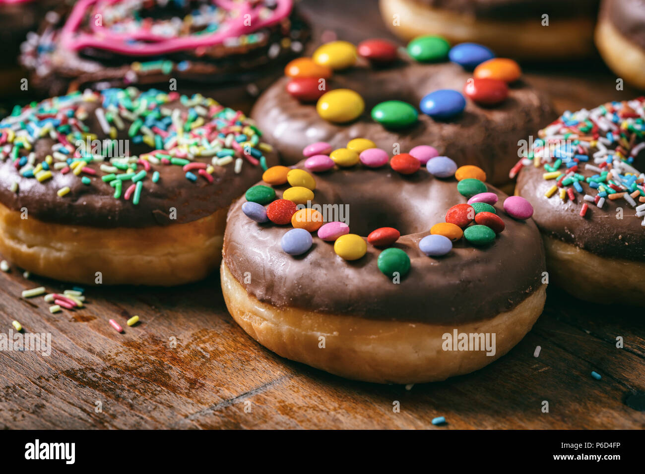 Pastries concept. Donuts with chocolate glaze and sprinkles, on wooden table blurry background. Stock Photo