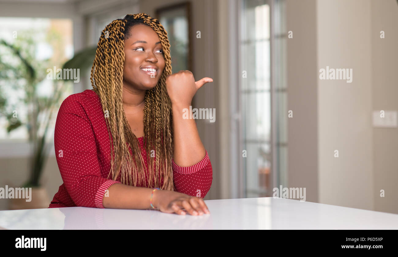 African american woman sitting at home pointing with hand and finger up ...