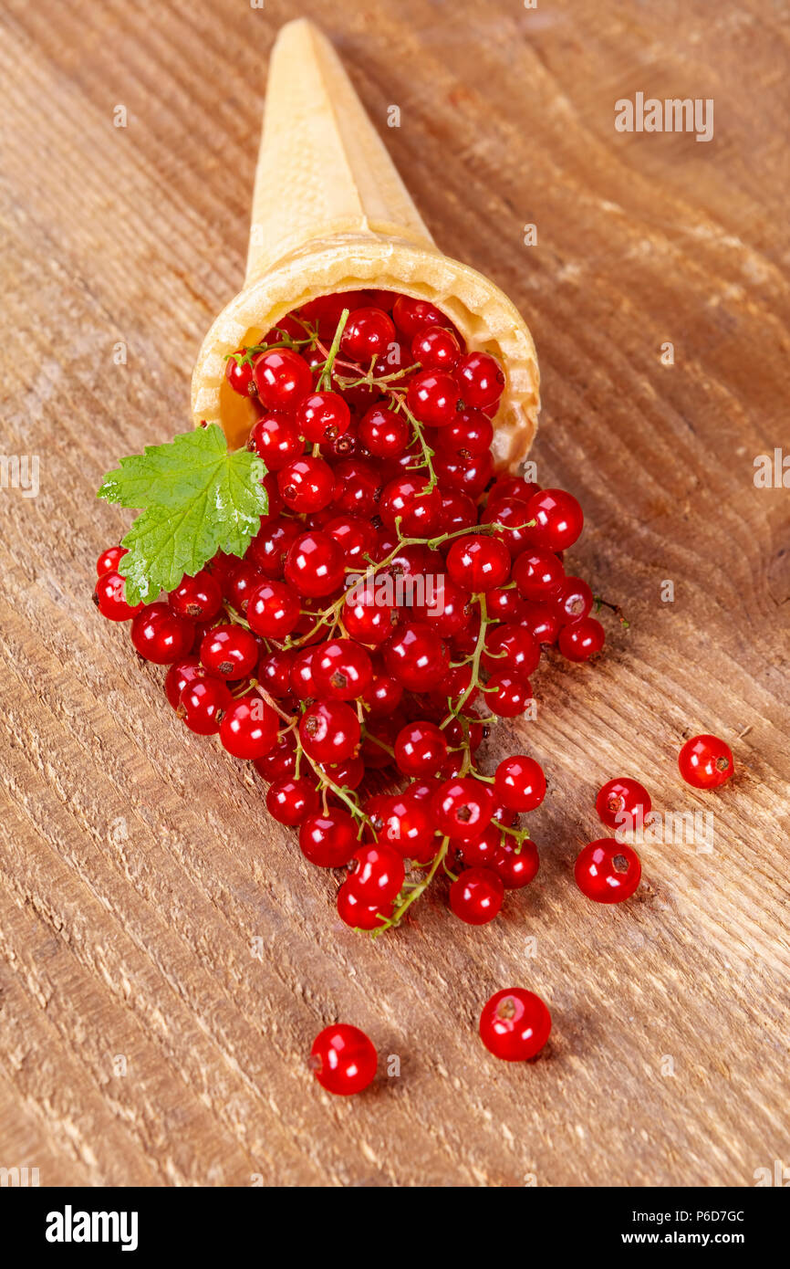 Red currant fruits in ice cream cone on wooden table. Focus on redcurrant. Stock Photo