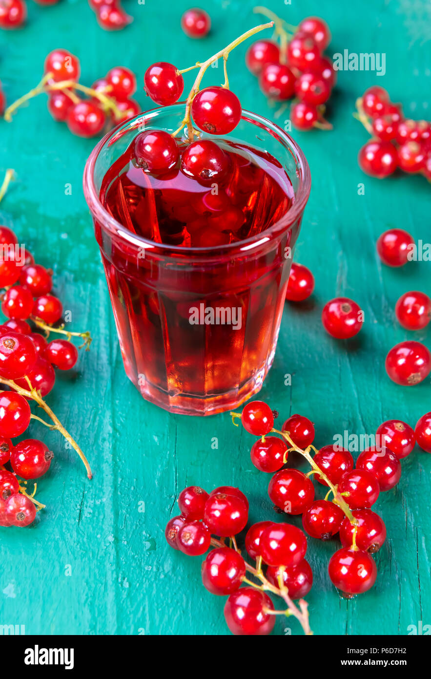 Redcurrant and glass with fruits and drink juice on wood table. Focus on redcurrant in glass, Stock Photo