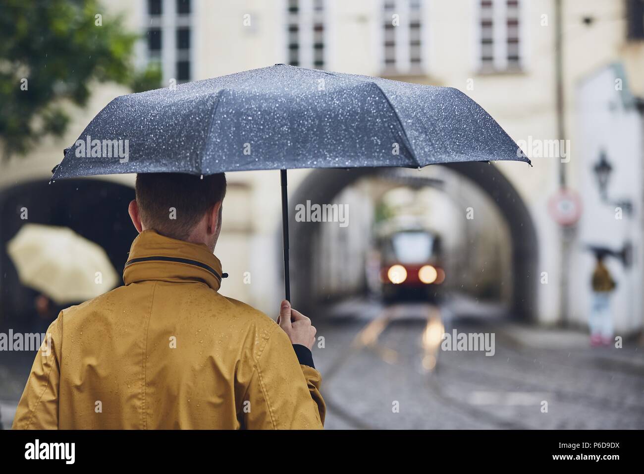 Young man holding umbrella walking in rain. Old city street in Prague, Czech Republic Stock Photo