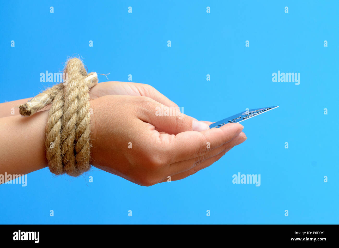 Women's hands tied with a rope and holding a credit card. Credit bondage. Stock Photo