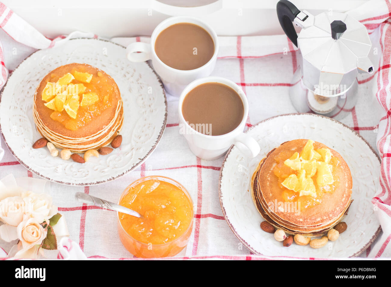 Romantic traditional breakfast for two on a tray. American pancakes with orange jam and nuts on vintage plates and 2 white coffee cups with italian me Stock Photo