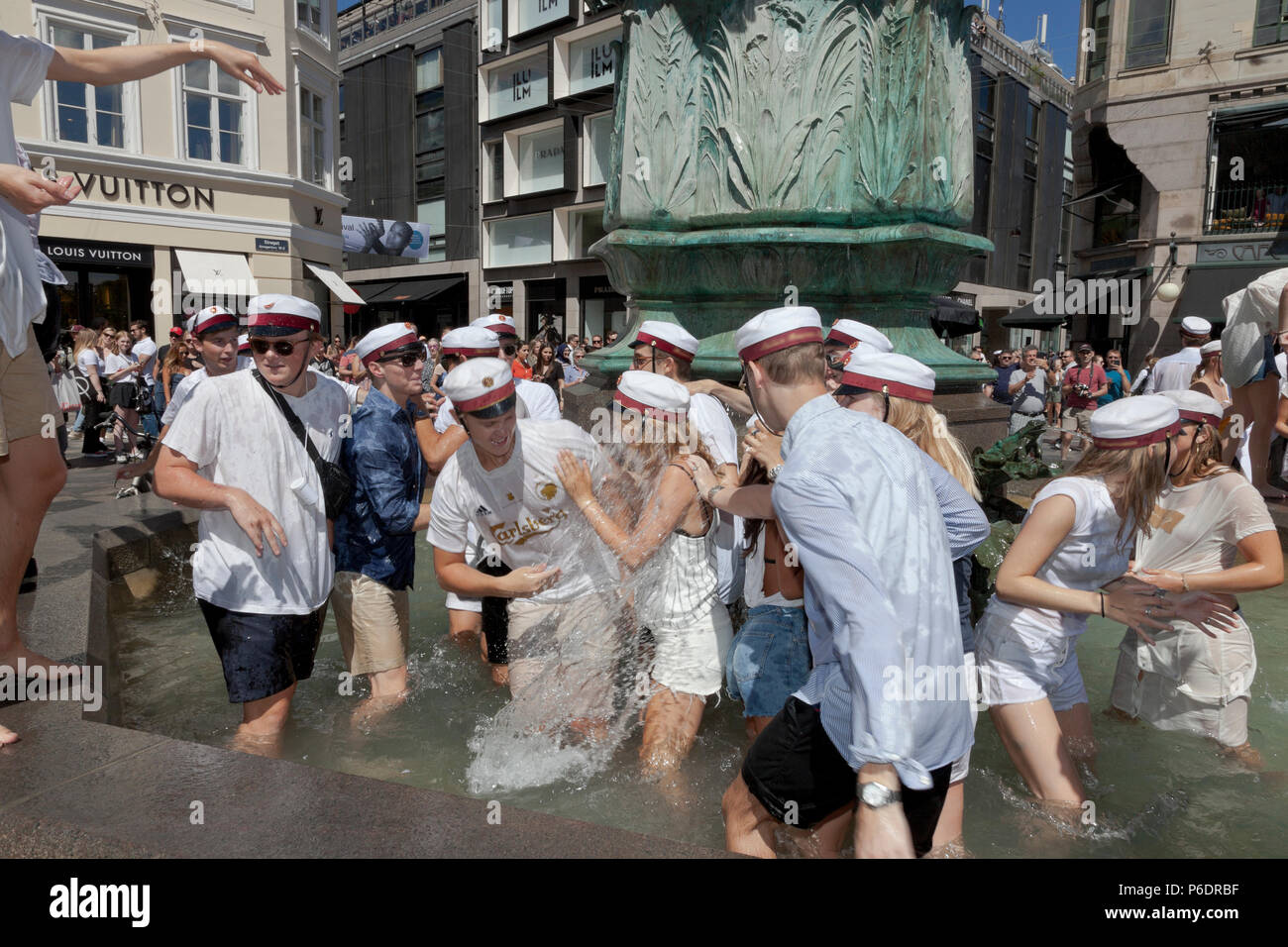 Copenhagen, Denmark. June 29, 2018. Happy, Danish students celebrate their high school, grammar school graduation and take the plunge. A dance around and a dip or dive into the cold water of the Stork Fountain (Storkespringvandet) on the pedestrian street, Stroeget, is a traditional element on the day of celebration for  graduated students in Greater Copenhagen. It is often part of the long, exhausting and high-spirited truck tour visiting each student’s home for refreshments. Credit: Niels Quist/Alamy Live News Stock Photo