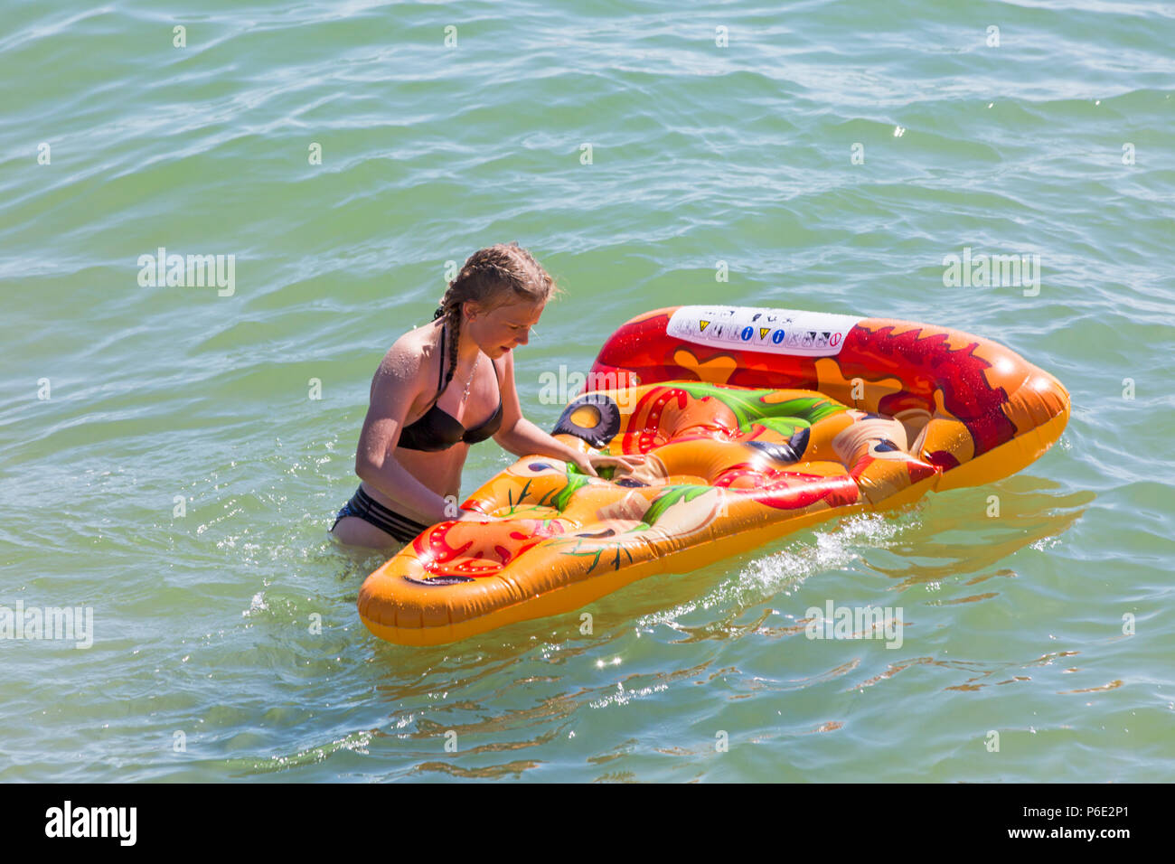 Bournemouth, Dorset, UK. 30th June 2018. UK weather: the heatwave continues and another hot sunny day at Bournemouth beaches as sunseekers head to the seaside. A slight breeze makes the heat more bearable. Piece of pizza? Young woman teen having fun cooling down in the sea with inflatable pizza. Stock Photo