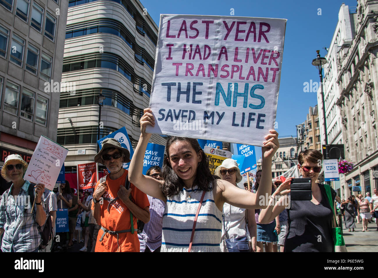 London, UK. 30 June, 2018. London,UK. A Young woman holds up her placard which reads " Last year I had a liver transplant, the NHS saved my life'. With the NHS 70 years old this year, thousands marched through central London in a National rally to show support for the service and to demand more funding from the Government. David Rowe/Alamy Live News Stock Photo