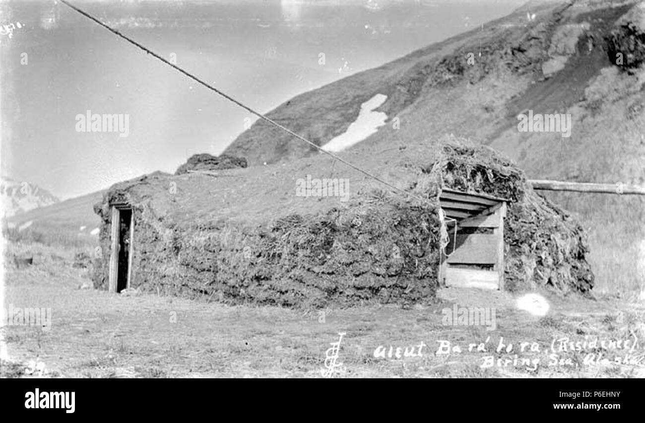. English: Aleut barabara, or sod hut, Akutan, Bering Sea, ca. 1912 . English: PH Coll 247.15 A barabara is a traditional Aleut home. Sod and grass are laid over a frame of whale ribs or wood covering an oblong pit. A barabara, pronounced buh-RAH-buh-ruh, blends into its surroundings quite well. The homes typically were 35 to 40 feet long and 20 to 30 feet wide. Aleuts entered the home by descending a pole ladder extending through the roof. A large common area in the middle was surrounded by sleeping areas along the walls. Sometimes graves were also dug into the walls.A typical village on the  Stock Photo