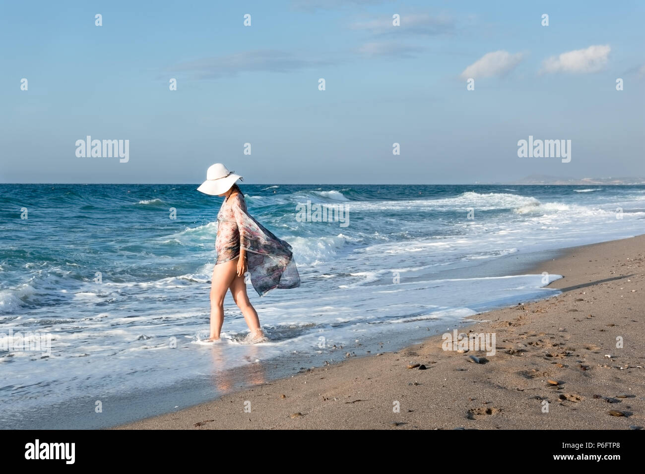 A woman with a white hat walks to the seaside beach on Crete Island Stock Photo