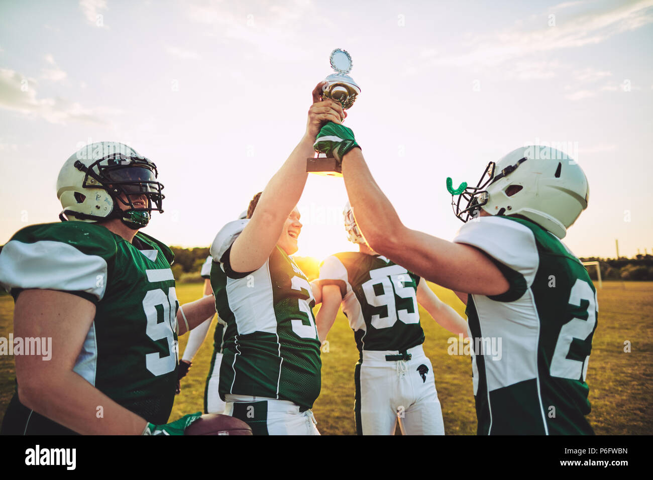 Excited group of young American football players raising a championship trophy together in celebration after a game Stock Photo