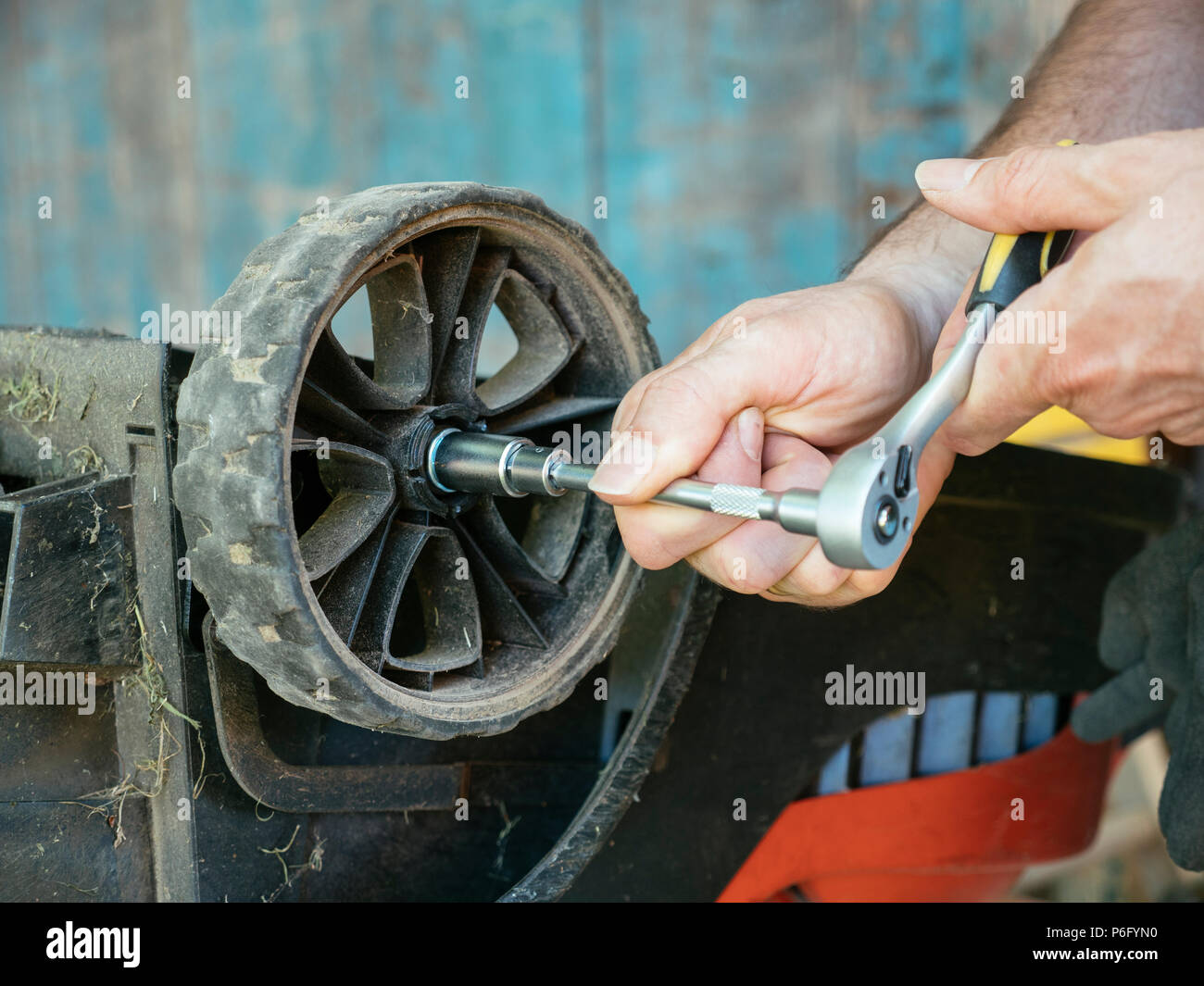 Man tightening a wheel on an electric lawn mower after repairing the axis. Stock Photo