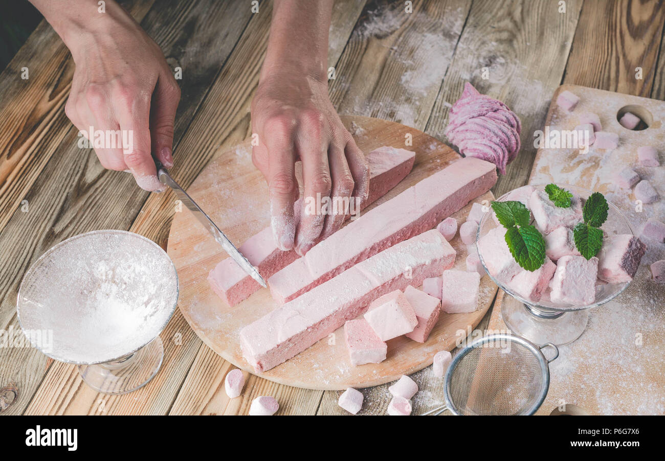 The confectioner cuts a strawberry marshmallow with a knife. Homemade sweet dessert. People at work Stock Photo