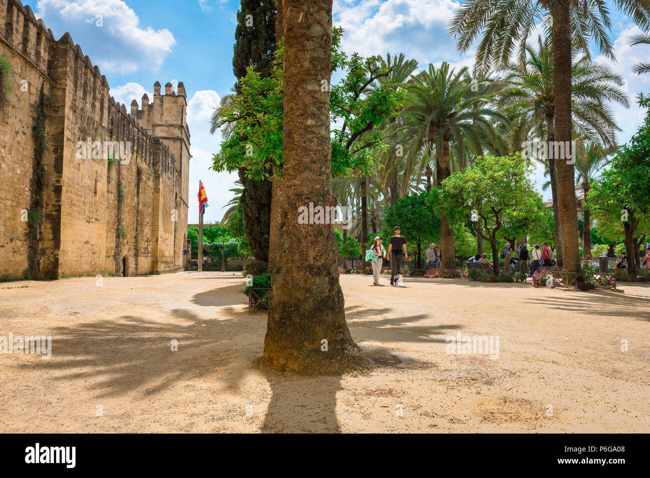 Andalucia Spain summer, a young couple stroll through a palm tree lined square outside the Alcazar de los Reyes Cristianos in Cordoba, Spain. Stock Photo