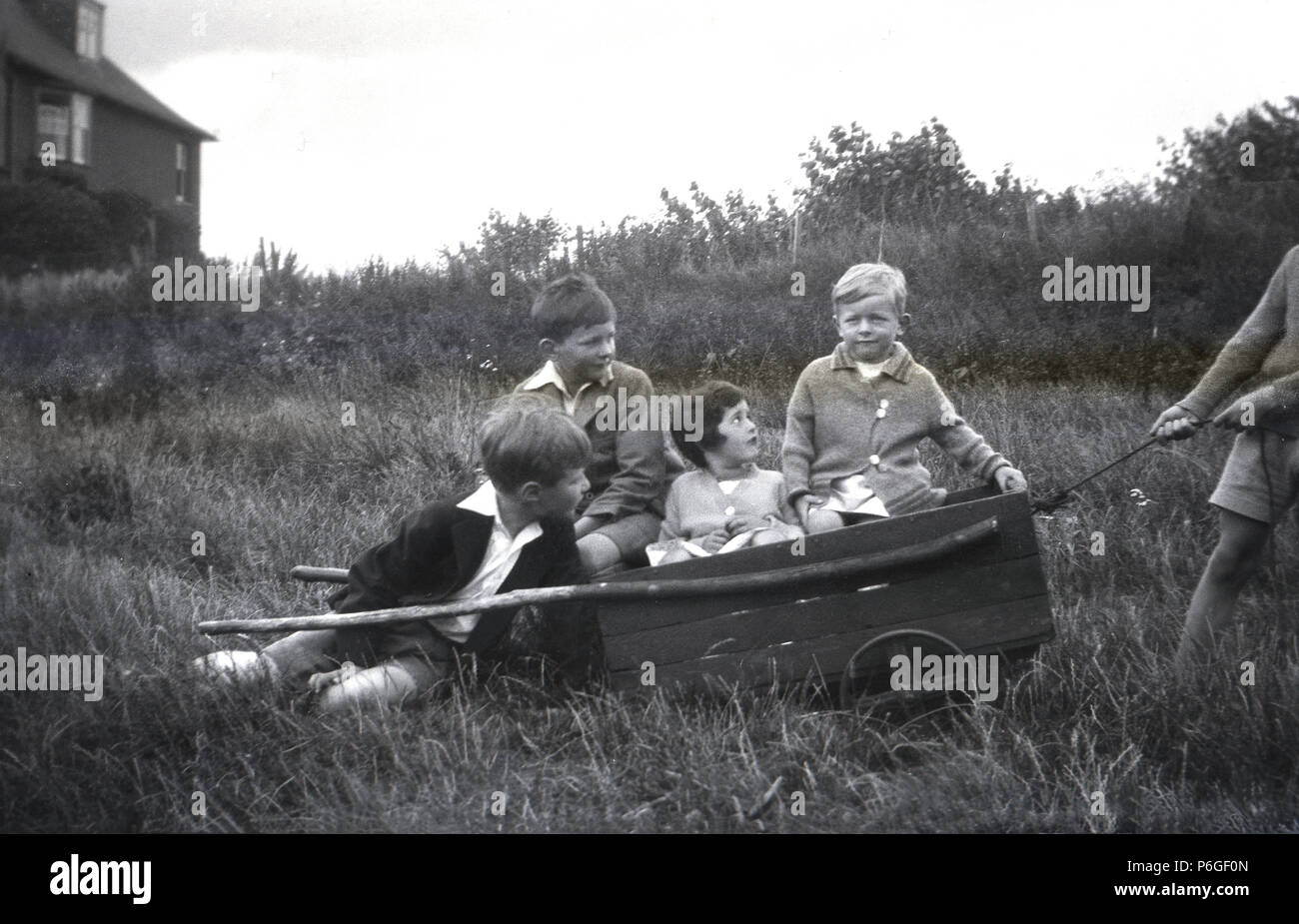 1950s, children outdoors in a grassy field sitting together in a small wooden handcart, England, UK. In this, era children had the freedom to play and roam outside, unsupervised, for hours on end and parks, fields, common land were places to play and have adventures with your friends. Stock Photo
