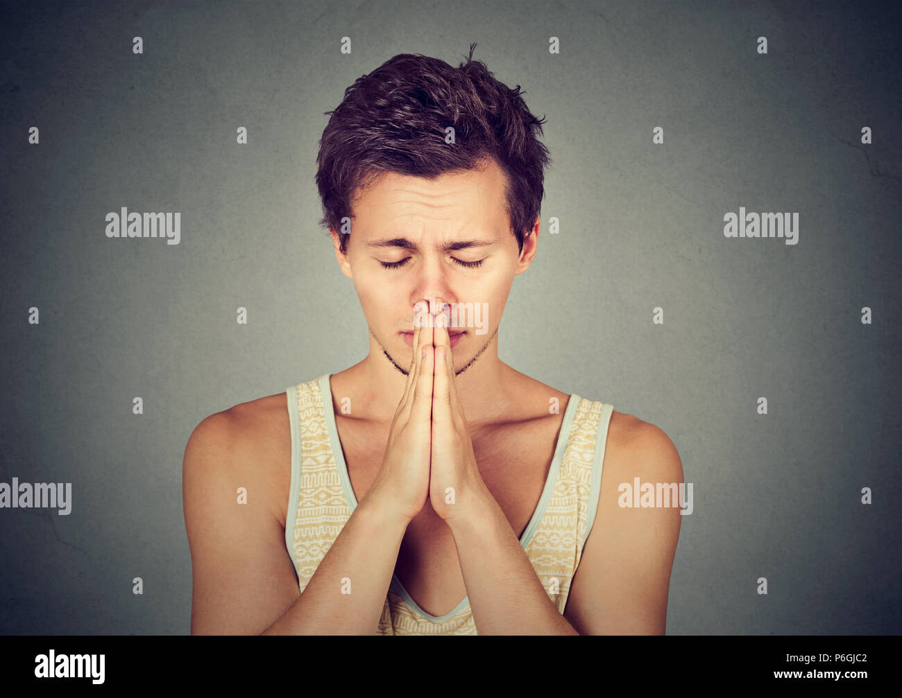 Young sad man holding hands together and eyes closed while praying