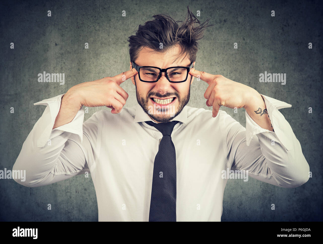 Young bearded man in stress holding fingers on temples and looking at camera in annoyance and disagreement Stock Photo