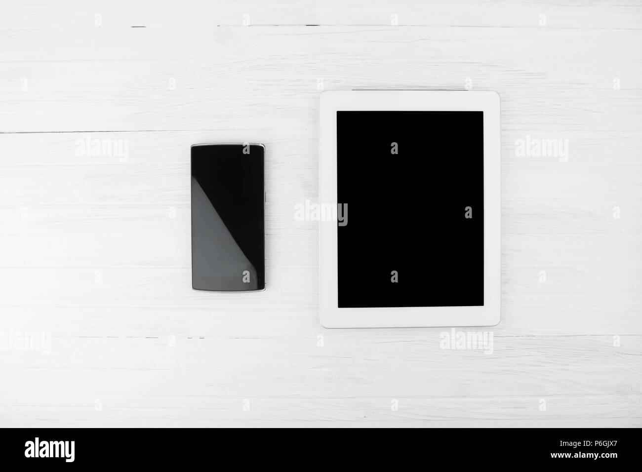 Big Black Empty Screen Smart Tablet Device Next To Smart Phone On White Wooden Background Top View Stock Photo