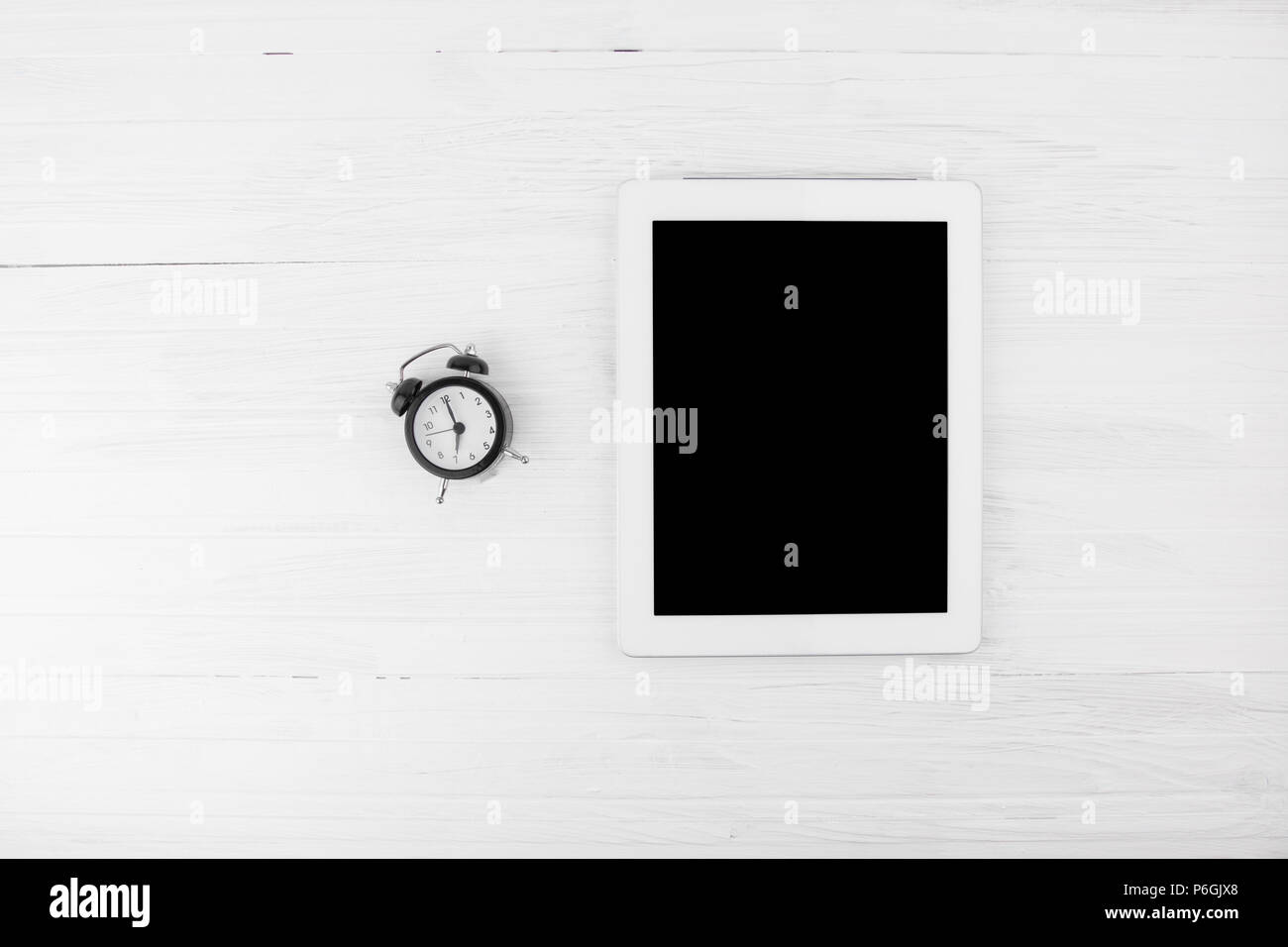 Big Black Empty Screen Smart Tablet Device Next To Bell Alarm Clock  On White Wooden Background Top Angle Stock Photo