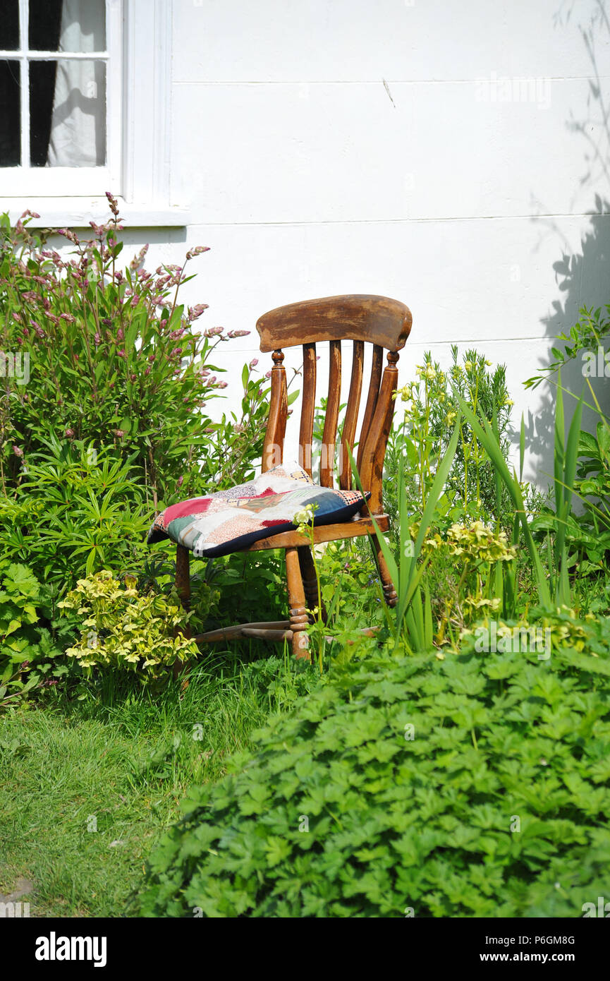 A single wooden chair by a cottage in a garden Stock Photo