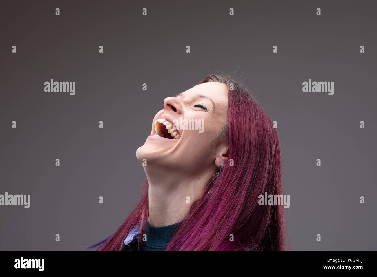 Laughing vivacious woman with modern dyed purple hair throwing back her