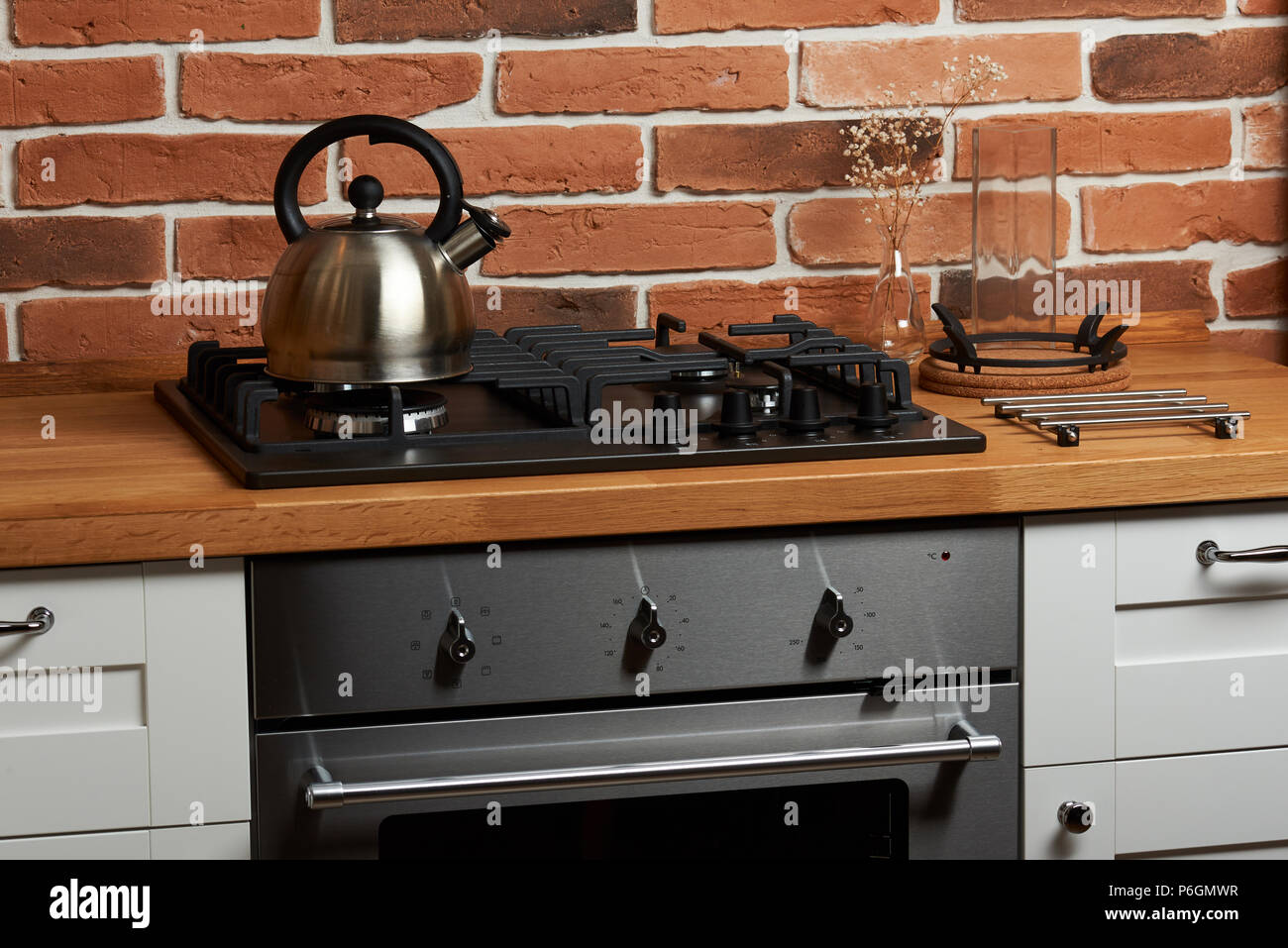 Metal kettle in modern kitchen stove on red brick background Stock Photo