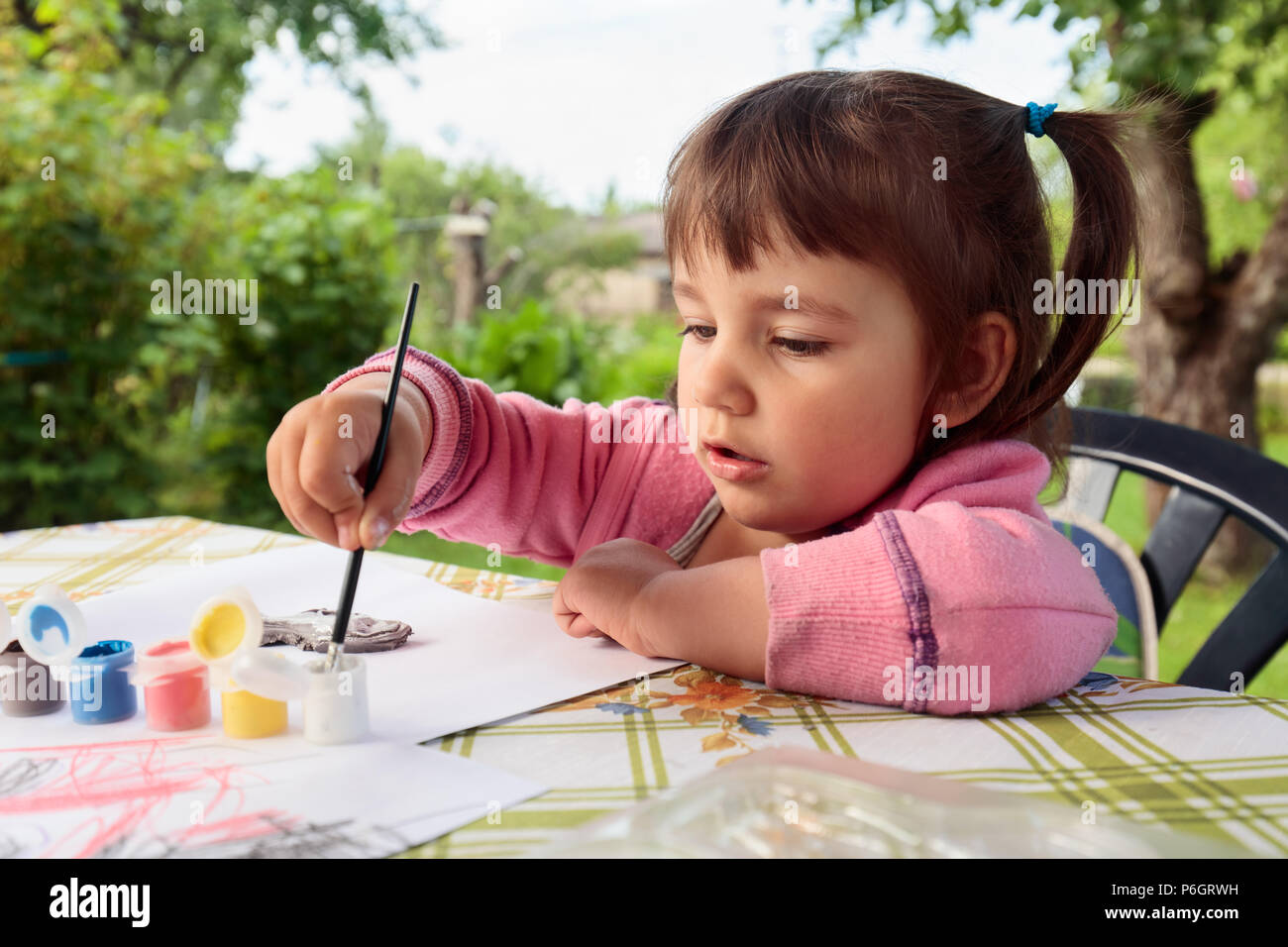 Cute little girl paints animal figures. Summer sunny day in the garden ...