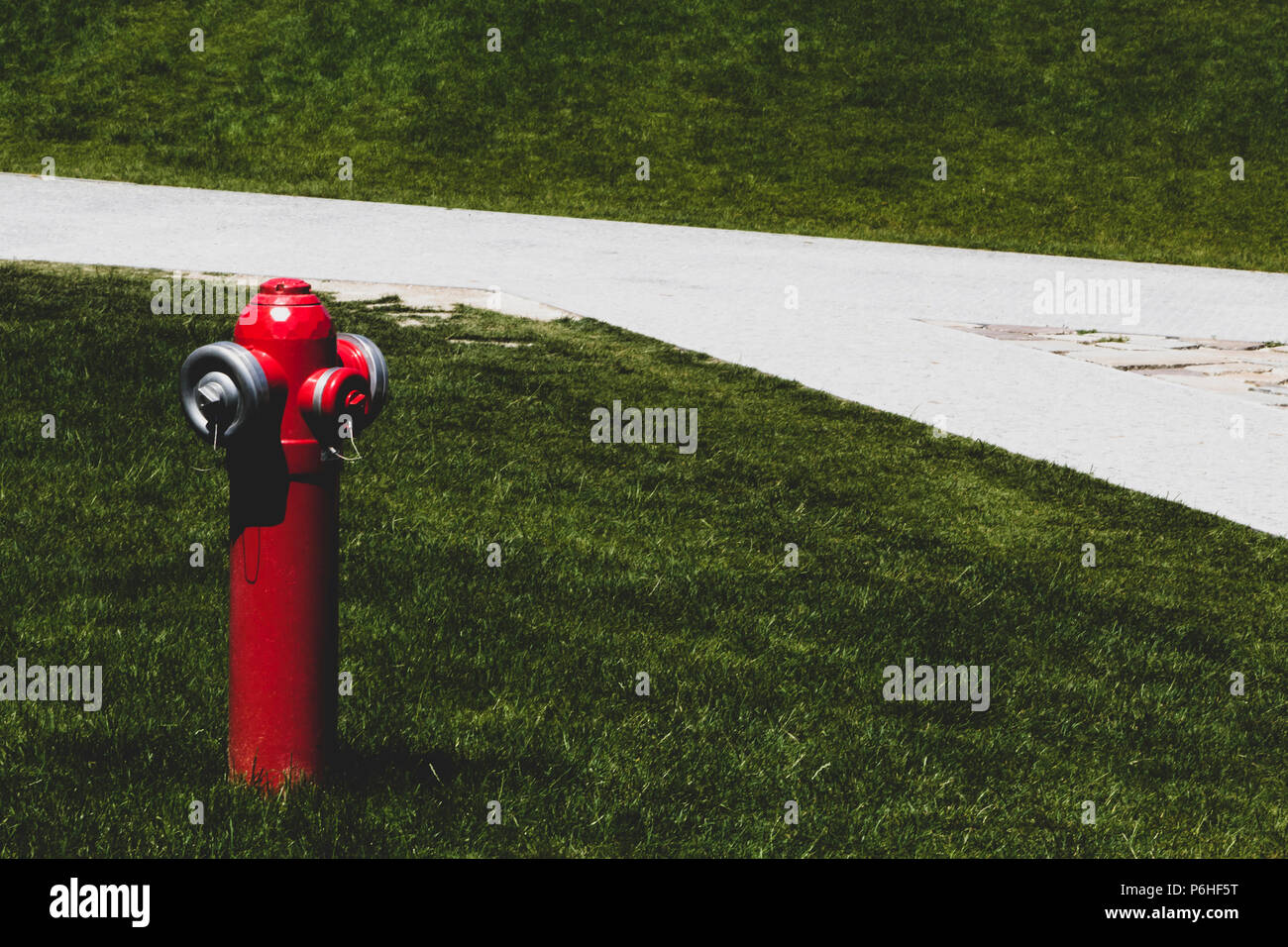 Red fire hydrant (pump) on green grass, in front of white walkway. Stock Photo