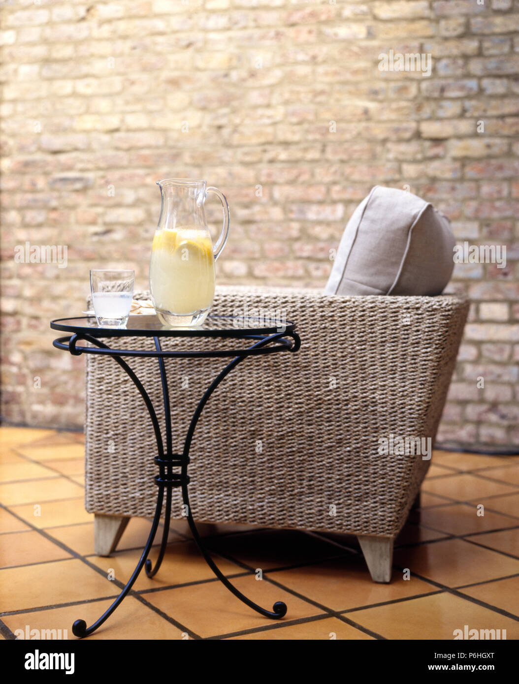 Small metal table beside a sisal upholstered sofa in living room with  exposed brick wall and terracotta tiled floor Stock Photo