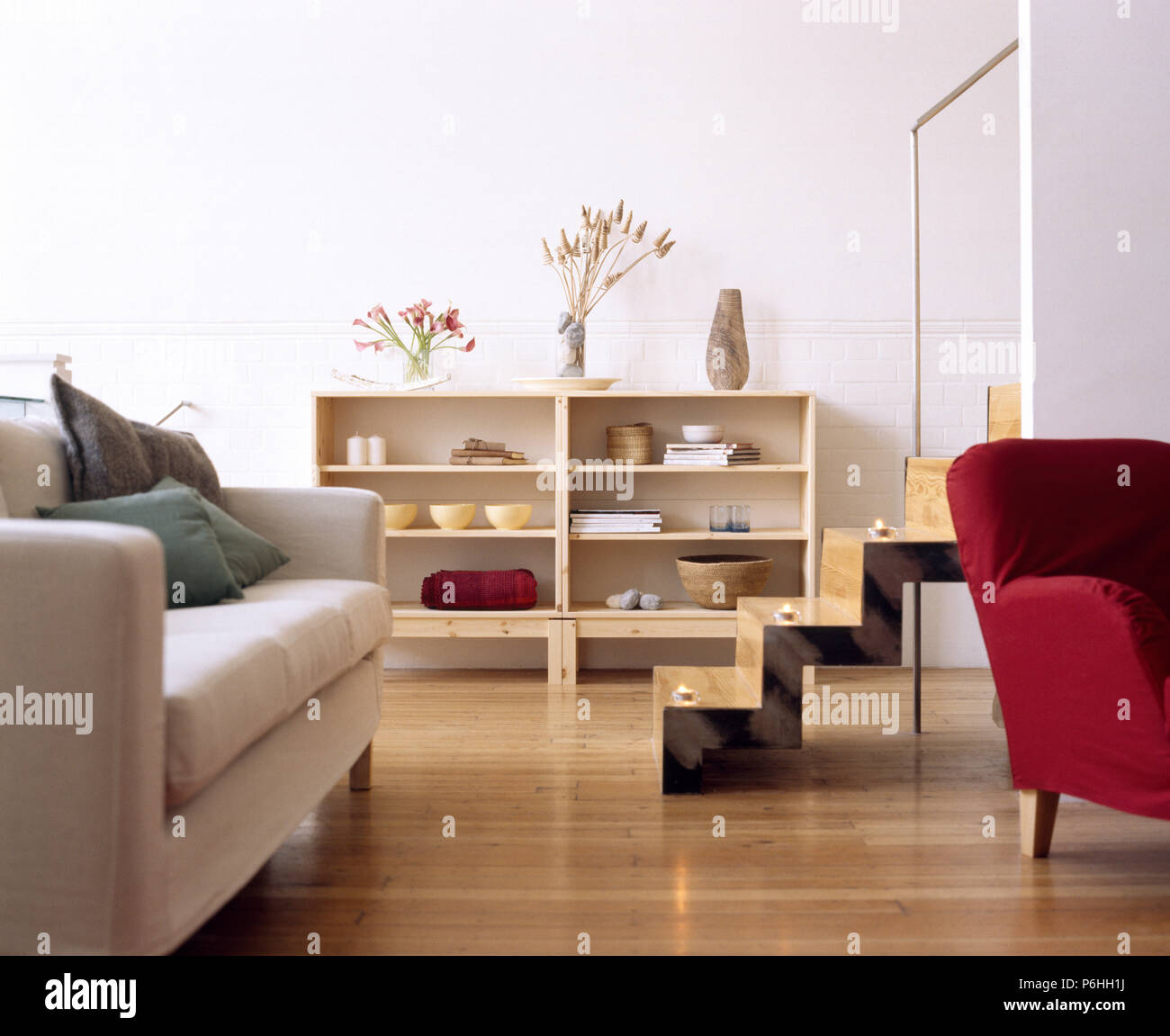 White sofa and red chair in a modern urban living room with wooden floor and shelving and a wooden staircase Stock Photo
