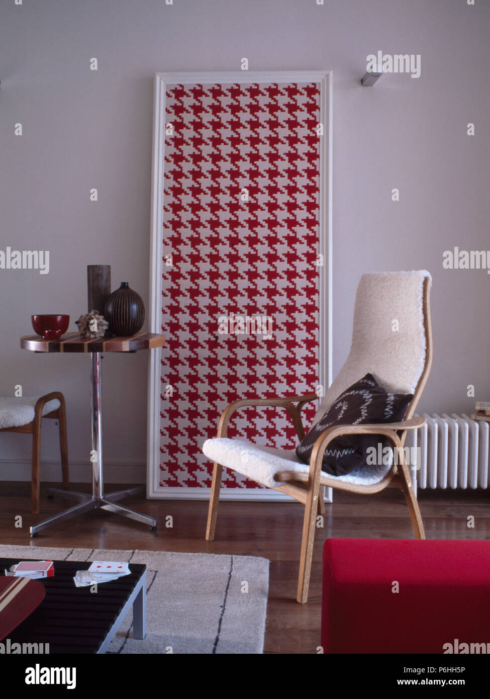Small circular pedestal table and large red+white houndstooth picture in living room with wooden-framed chair Stock Photo