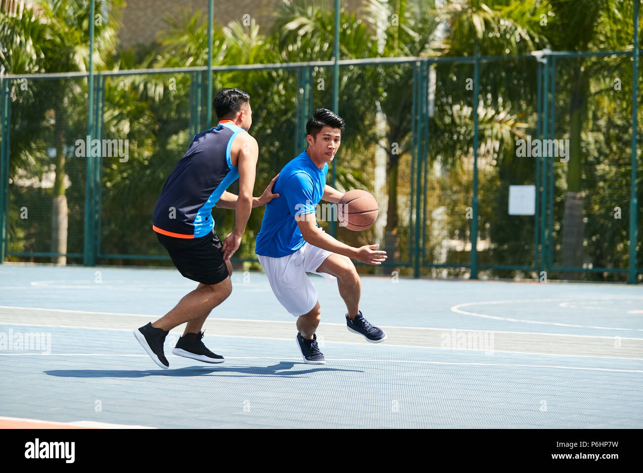 young asian male basketball player playing one-on-one on outdoor court. Stock Photo