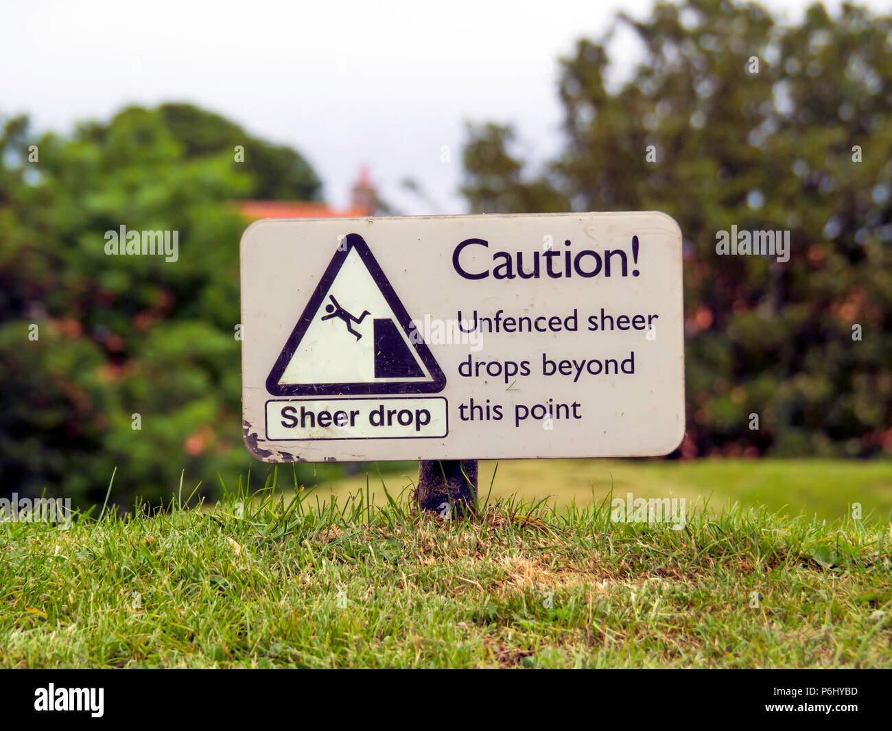 Sign on a grassy bank warning of a sheer drop Unfenced Sheer Drops Beyond This Point Stock Photo