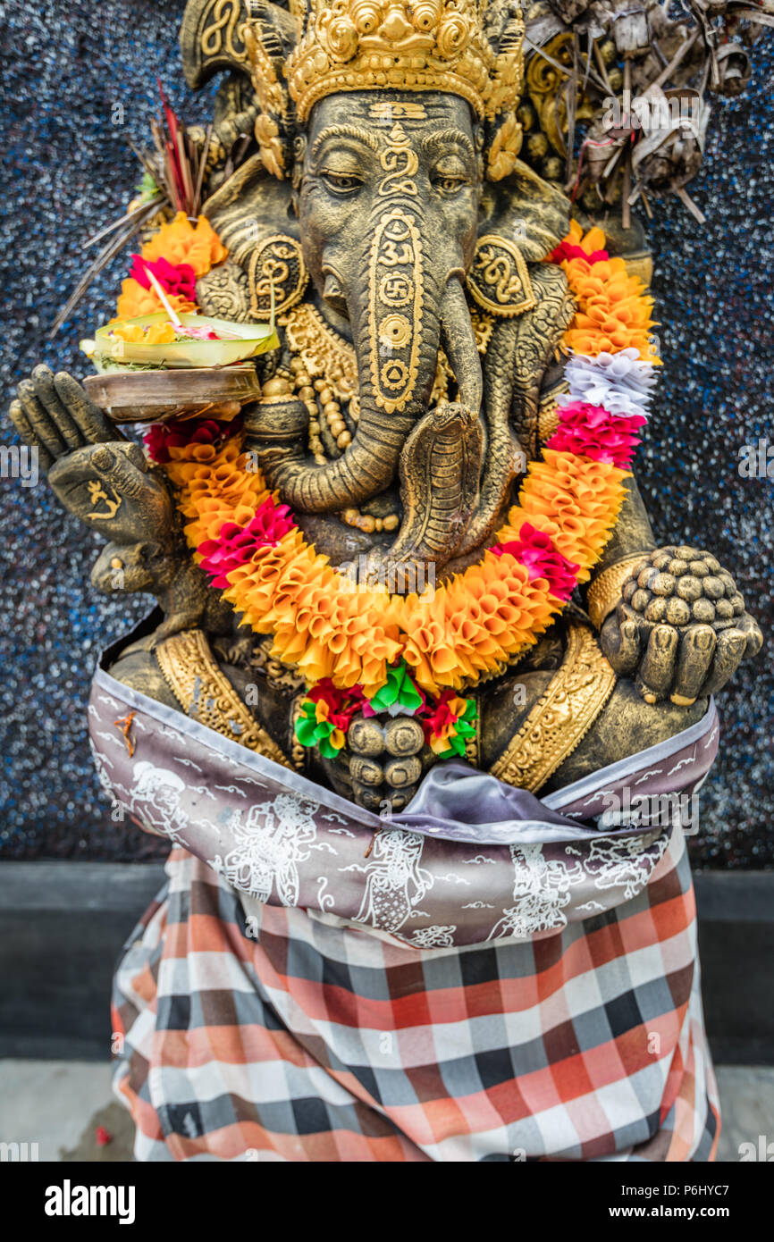 Ganesha Hindu statue in a flower necklace and traditional Balinese sarong near a local house, Nusa Lembongan, Indonesia Stock Photo