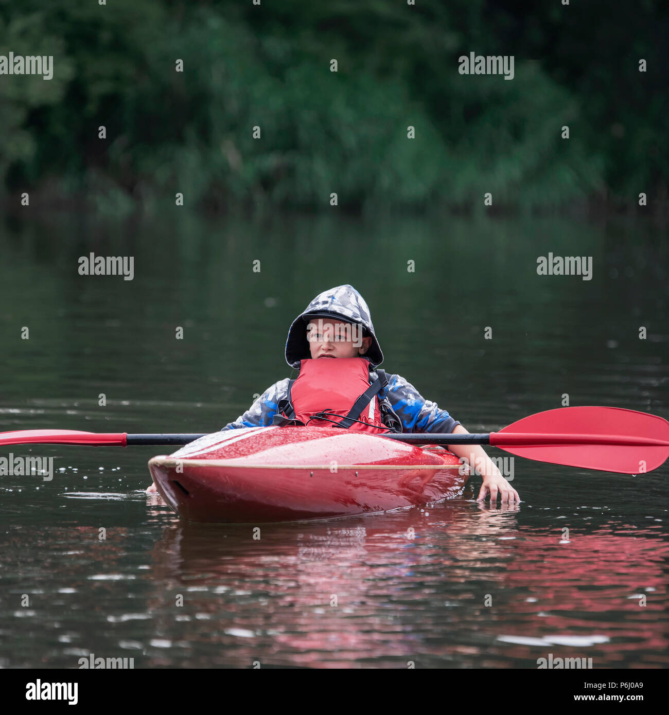 teenager boy in a tail boat kayak put his oar on the boat and tiredly dropped his hands into the river, drifting along the river Stock Photo