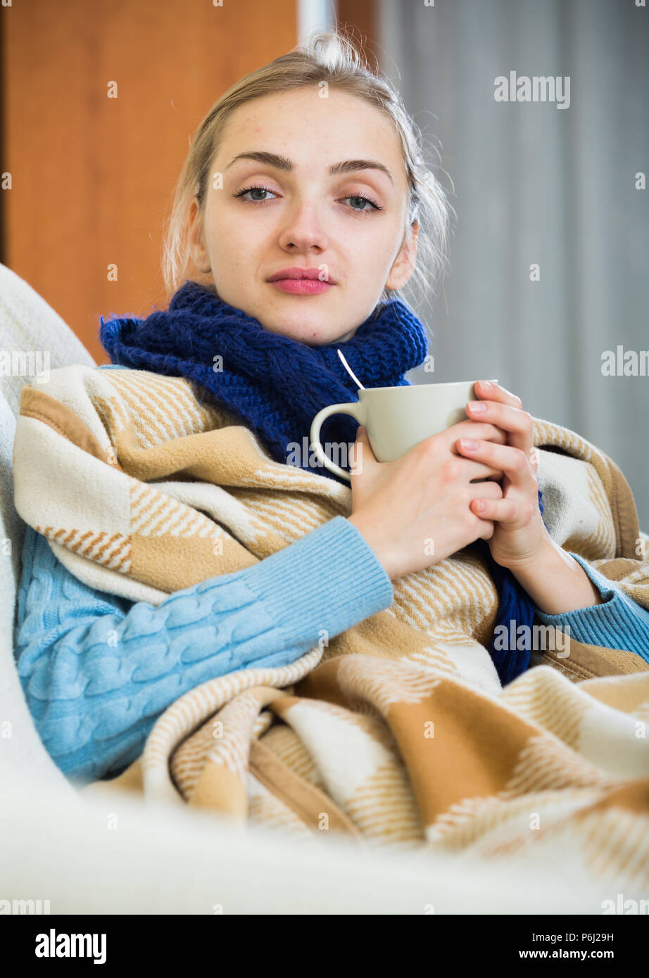 Sick female with fever wrapping herself in blanket and smiling Stock