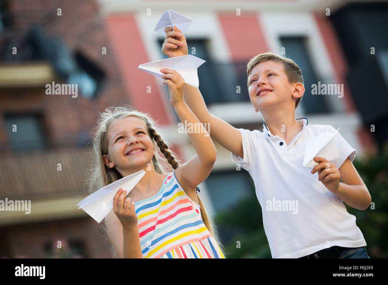 two happy kids playing with simple paper planes on sunny day in town ...