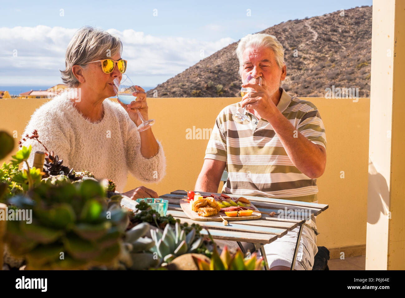 senior adult couple outdoor on the rooftop drinking somw white wine and eating some snacks food salds and fruits. sunny day of vacation or retired lif Stock Photo