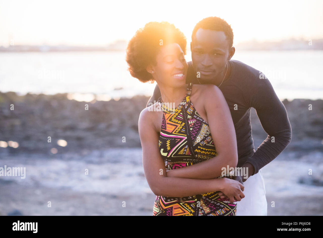 beautiful couple of black race african models in traditional dress have fun and love together at the beach in summer during the sunset. nice backlight Stock Photo