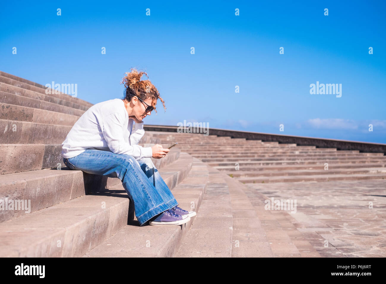 lonely middle age woman at work with a smartphone sitting on a long beautiful staris in urban contest. leisure with tehnology concept for modern lady Stock Photo