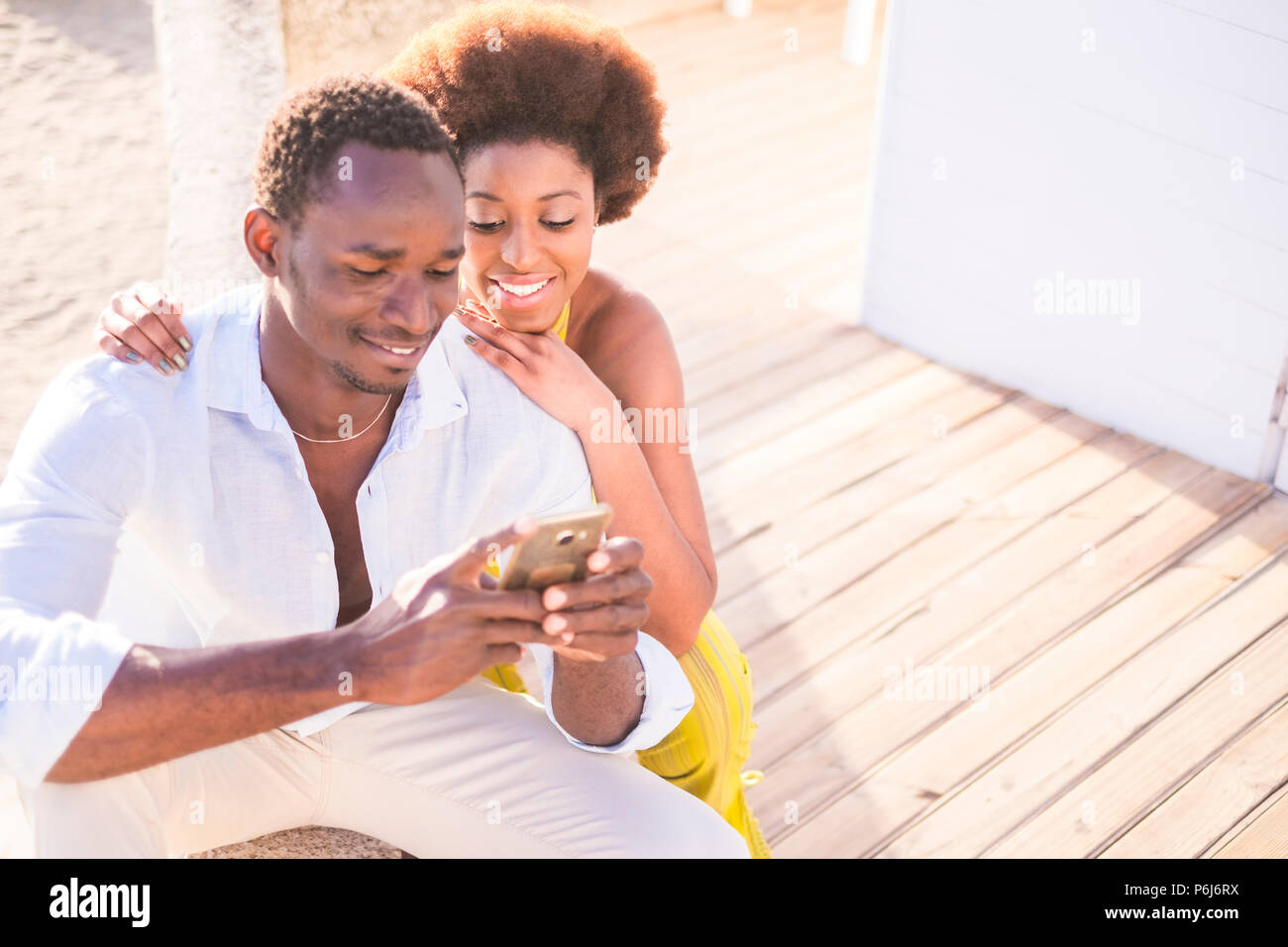 beautiful couple of black race african models use the smartphone together in friendship smiling and enjoying the contents. connected with friends or l Stock Photo