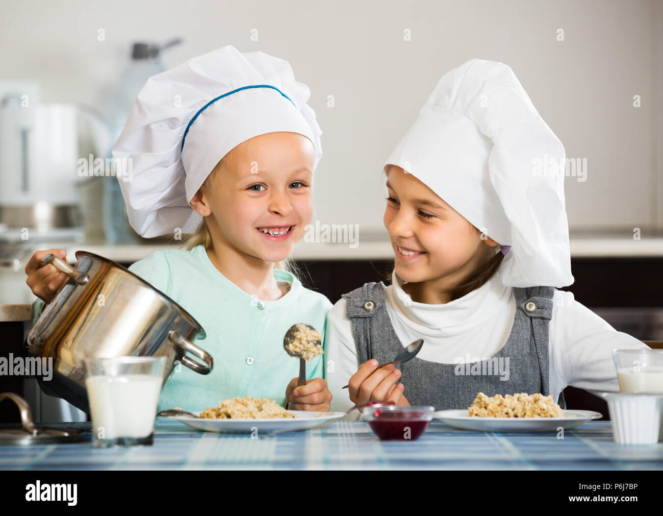 Two positive small girls eating healthy oatmeal in kitchen Stock Photo