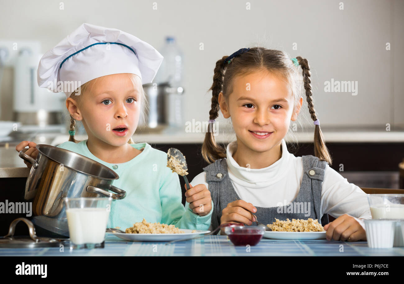 Portrait of happy little sisters eating tasty porridge in kitchen Stock Photo